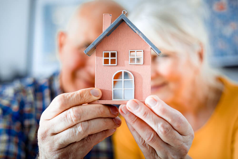 senior-couple-holding-house-model-1451189576 (1)