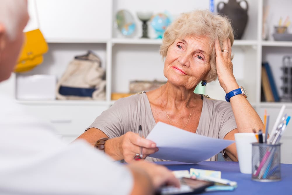 Upset,Senior,Woman,Sitting,At,Home,Table,Discussing,With,Husband